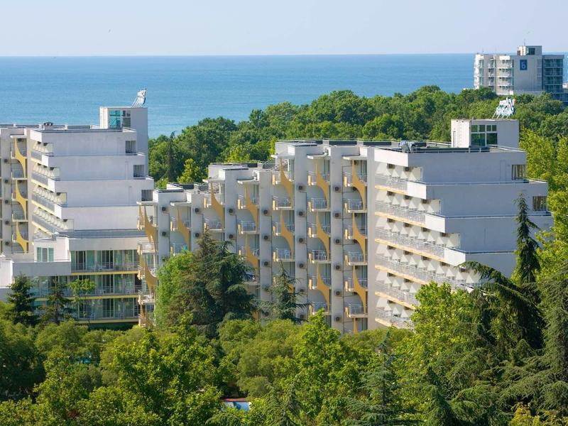 Meerverdiepingen hotelgebouwen met balkons voor een bebost kustgebied en zee op de achtergrond
