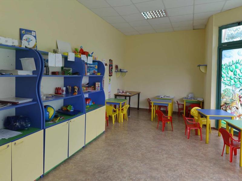 Speelkamer voor kinderen met kleurrijke tafels en stoelen naast een raam met uitzicht naar buiten.