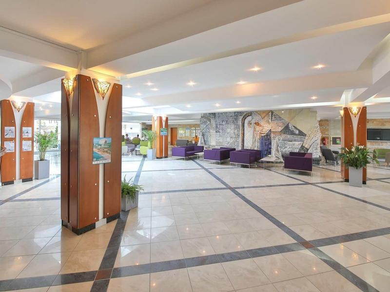 Ruim hotel lobby met marmeren vloer, zithoeken en grote zuilen.