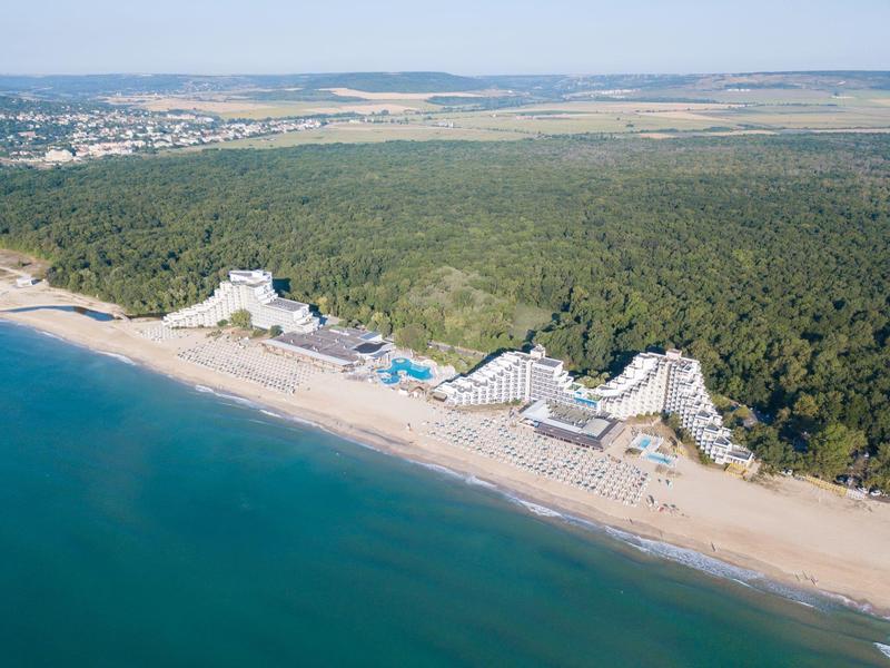 Luchtfoto van een hotel aan een bosrijke zandstrand met uitzicht op de zee.