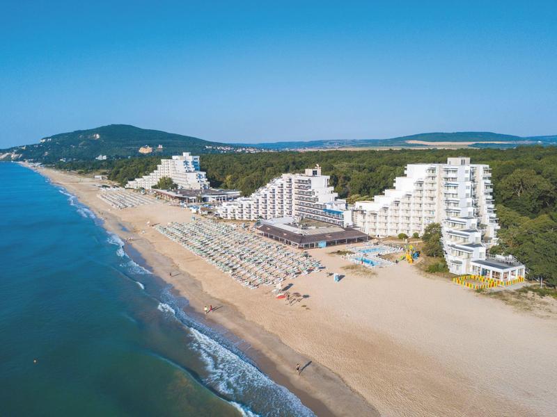 Strandhotel met witte architectuur en ligstoelen op zandstrand onder blauwe lucht.