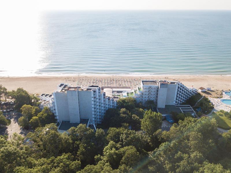 Hotelgebouwen aan een beboste kust met strand en kalme zee op de achtergrond