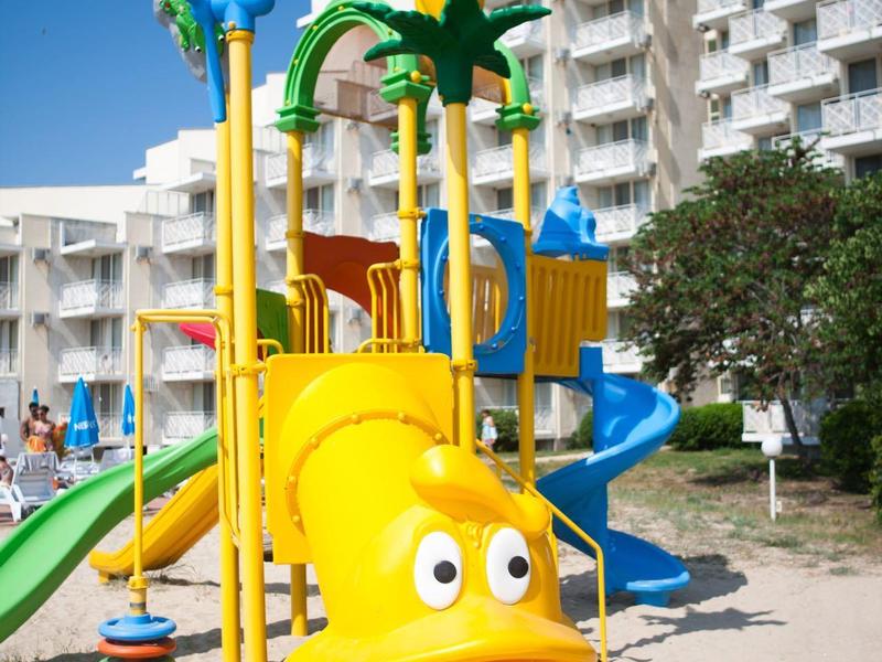 Kleurrijke speeltuin met glijbanen voor een hotelgebouw bij een blauwe lucht.