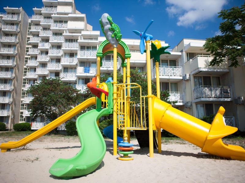 Kleurrijke speeltuin met glijbanen voor een modern hotelgebouw bij zonnig weer.