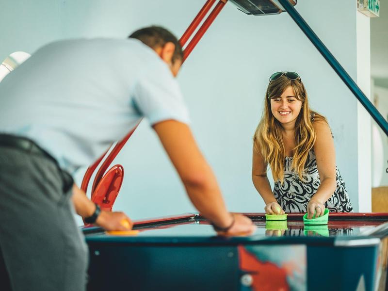 Twee mensen spelen vrolijk biljart in een lichte kamer van een vakantieresort.