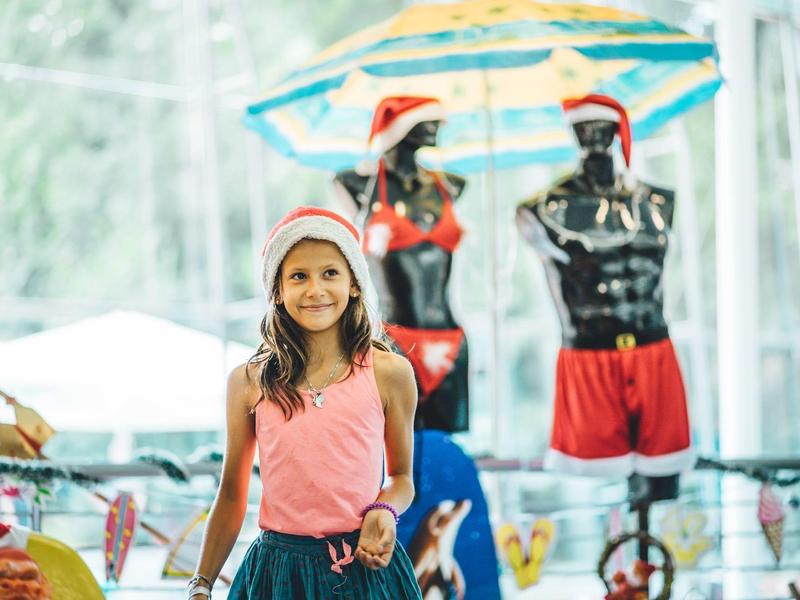 Meisje met kerstmanmuts in een winkel met zwemkleding en strandparaplu op de achtergrond.