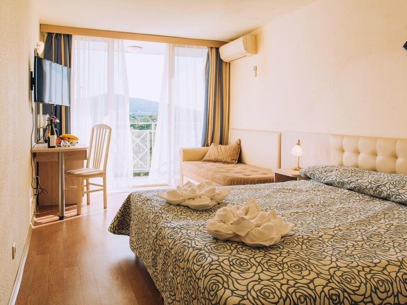 Lichte hotelkamer met tweepersoonsbed, bureau, tv en balkon met uitzicht op de bergen.