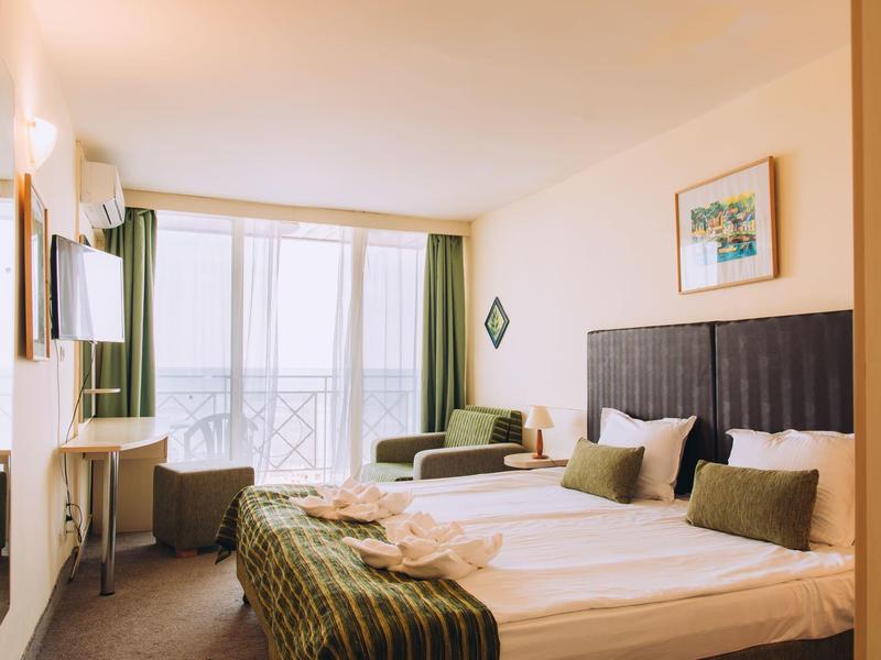 Lichte hotelkamer met twee bedden, groene bank, bureau en groot raam met gordijnen.