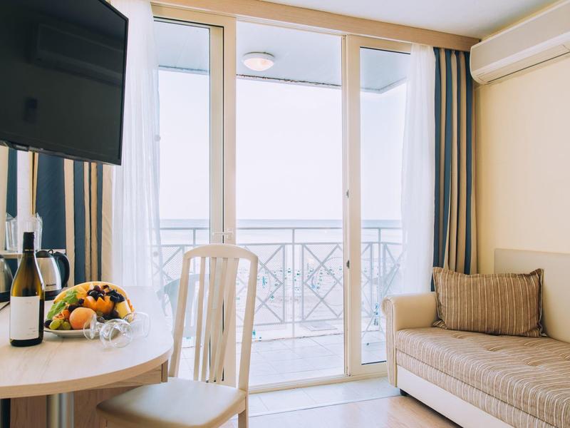 Lichte hotelkamer met balkon, bank, stoelen, tafel, tv en fruitmand