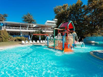 Piscina para niños con estructura de juego colorida frente a un edificio de hotel bajo cielo azul.