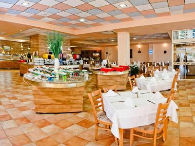 Restaurante luminoso con mesas preparadas y estaciones de buffet sobre suelo de baldosas.