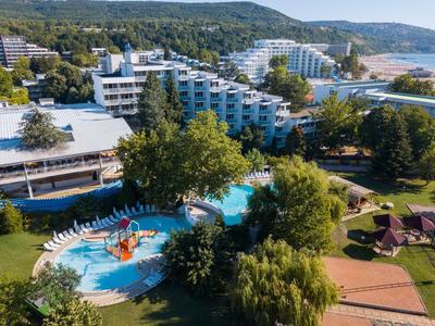 Hotelgelände mit Schwimmbad, Liegestühlen, grünen Bäumen und Hügeln im Hintergrund.