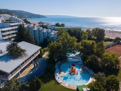 Complejo hotelero con piscina, árboles y vista a una playa y el mar al fondo.