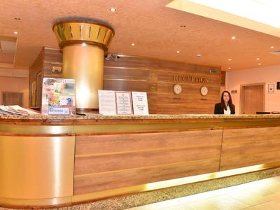 Recepción en un hotel con una recepcionista detrás del mostrador de madera con detalles dorados.