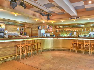 Acogedor bar de hotel con barra de madera y taburetes, iluminado por luces cálidas en el techo.