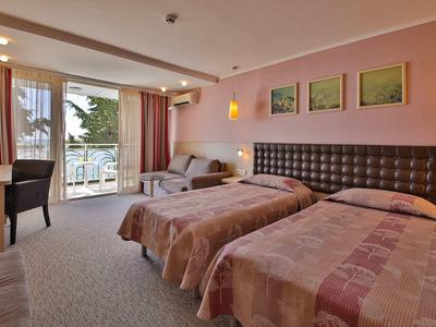 Habitación de hotel con dos camas individuales, escritorio, silla y balcón con vista a la naturaleza.