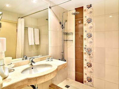 Baño de hotel luminoso con doble lavabo, espejo de pared y ducha tipo walk-in con cortina.