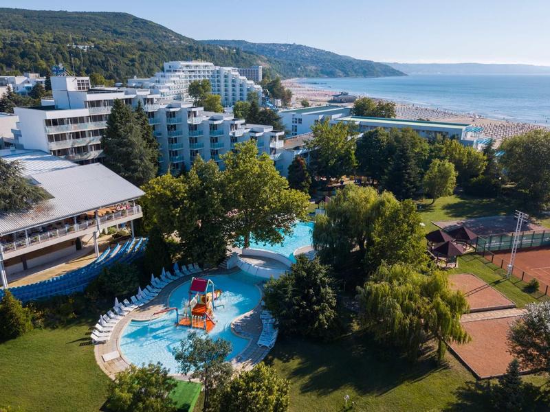 Complejo hotelero con piscinas, terraza soleada y playa en un entorno costero pintoresco.