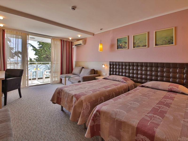 Habitación de hotel con dos camas individuales, escritorio, silla y balcón con vista a la naturaleza.