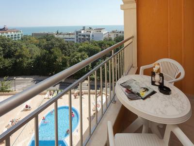 Balcony with white table and chairs, overlooking pool and buildings by the sea.