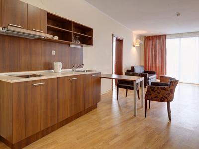 Modern hotel kitchen with wooden cabinets, dining table, and chairs in a bright room.