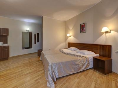 A simply furnished hotel room with double bed, wooden floor, and wall lighting.