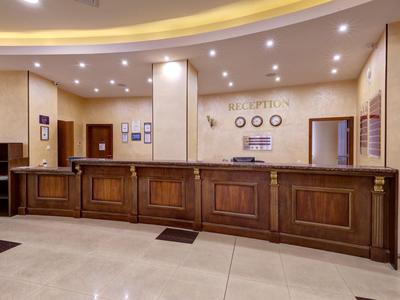 Reception with dark wooden counter, beige walls, and ceiling lights in the hotel.