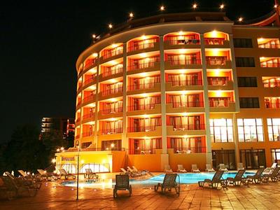 Modern hotel with illuminated balconies and pool area at night.