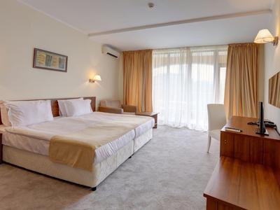 Bright hotel room with double bed, desk, and large windows with curtains.