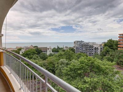 Balcony overlooking green trees, buildings, and the sea under a cloudy sky.