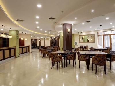 Large hotel dining area with tables and chairs, bright lighting, and open layout.