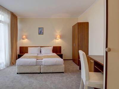 Bright hotel room with double bed, nightstands, wardrobe, and desk.