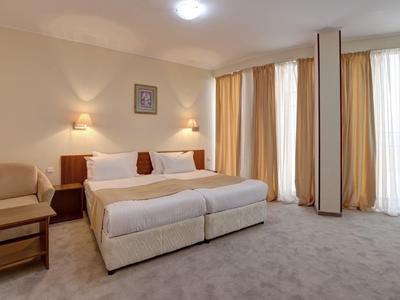 Bright hotel room with double bed, two nightstands, and large windows with curtains.