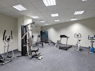 A modern gym with treadmills, bikes, and strength machines on carpeted floor.