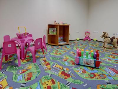 Children's playroom with colorful carpet, small chairs, tables, toys, and rocking horse.