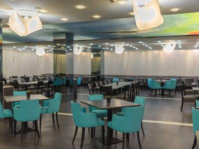 Modern breakfast room with blue chairs and black tables in a hotel.
