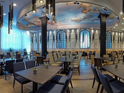 Elegant restaurant with high ceilings, painted dome, and modern furniture in warm lighting.