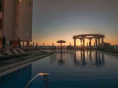 Hotelový bazén s lehátky a altánem při západu slunce.