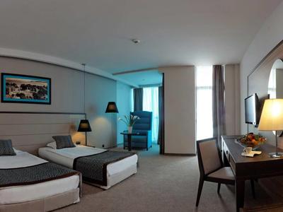 Moderní hotelový pokoj se dvěma jednolůžky, psacím stolem a posezením u okna.