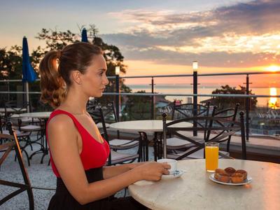 Woman sits at an outdoor table with coffee and juice at sunset by the water.