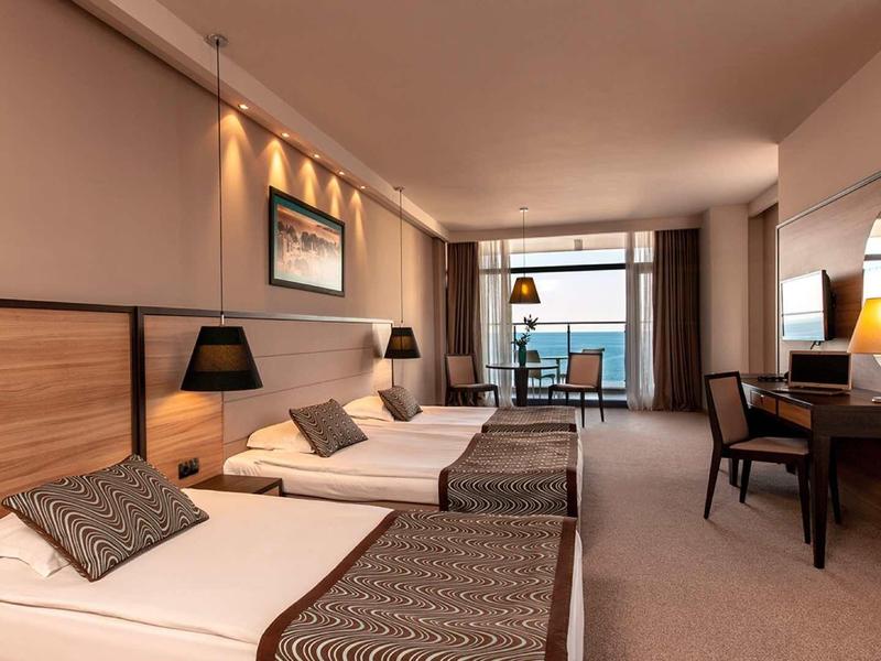 Moderní hotelový pokoj se dvěma jednolůžky, psacím stolem a balkonem s výhledem na moře.