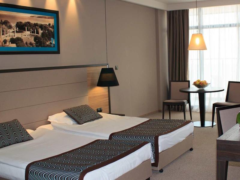 Moderně zařízený hotelový pokoj se dvěma jednolůžky, psacím stolem a posezením za denního světla.