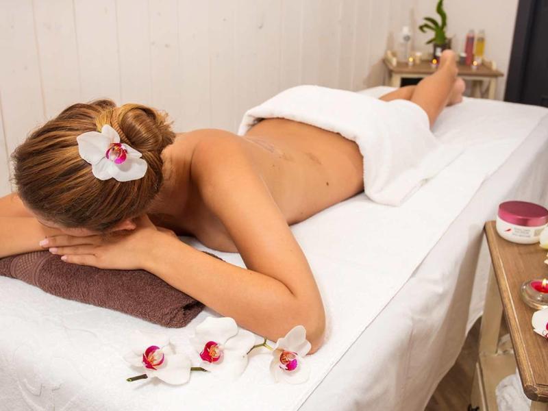 Žena leží uvolněně na masážním stole zakrytá ručníkem ve spa místnosti.