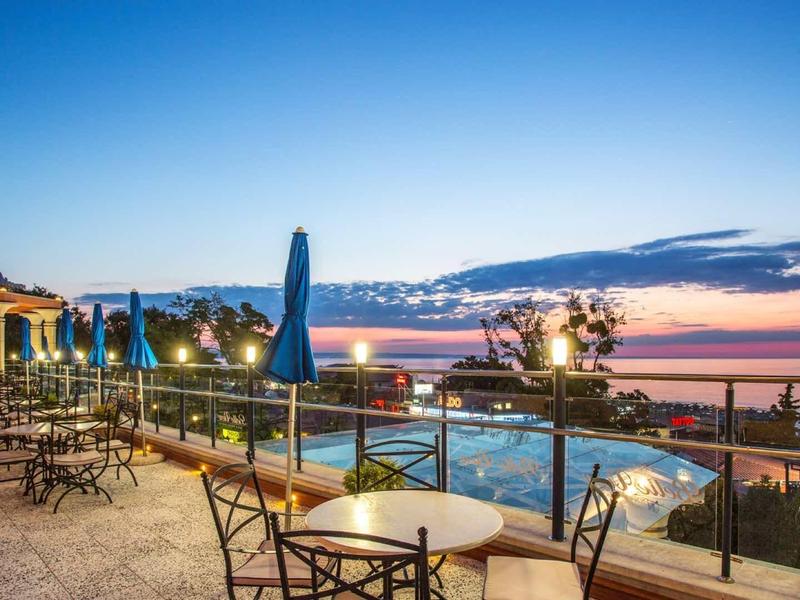 Terasa s stoly, židlemi a slunečníky při západu slunce s výhledem na moře a bazén.