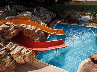 Deux toboggans mènent à une piscine bleue claire entourée de rochers et de nature.