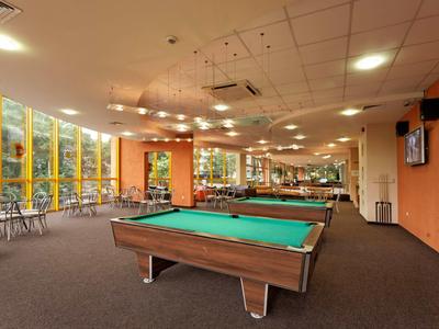 Espace intérieur avec tables de billard, murs orange et grandes fenêtres donnant sur des arbres.