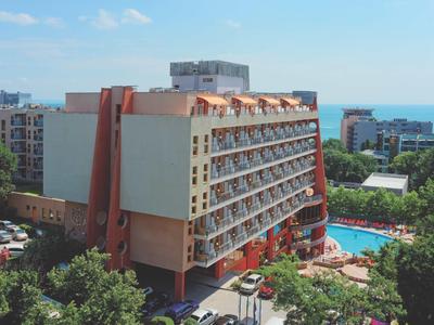 Velká hotelová budova s balkony vedle venkovního bazénu a hustou zelení.