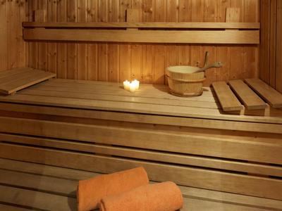 Pohodlná sauna s dřevěnými lavicemi, světlem svíčky a saunovými doplňky.