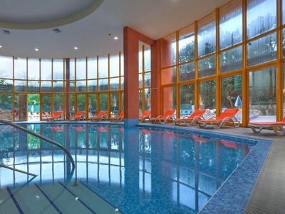 Vnitřní bazén s velkými okny a oranžovými lehátky vedle vody.