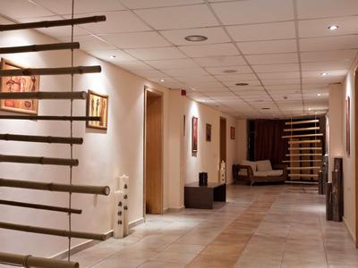 Un long couloir d'hôtel avec des murs blancs, des lumières au plafond et des escaliers en bois modernes de chaque côté.